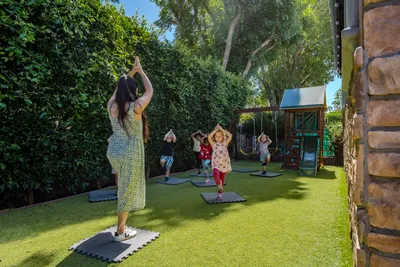 An instructor leading preschoolers in tree pose during outdoor yoga